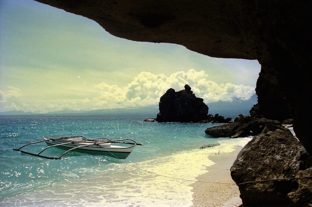A quiet cove on Apo Island, framed by a rock overhang, with a boat in the shallows
