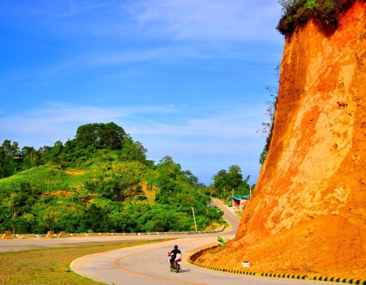 A bend of the Cebu Transcentral Highway with an orange road cut, green hills and blue sky, on the way to Balamban, 2011