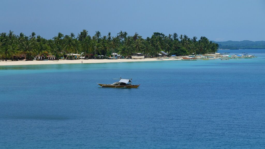 A bangka on calm blue water off Bantayan's palm-lined coast