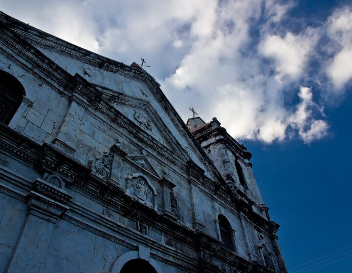 The basilica's stone front and bell tower seen from below against a blue sky