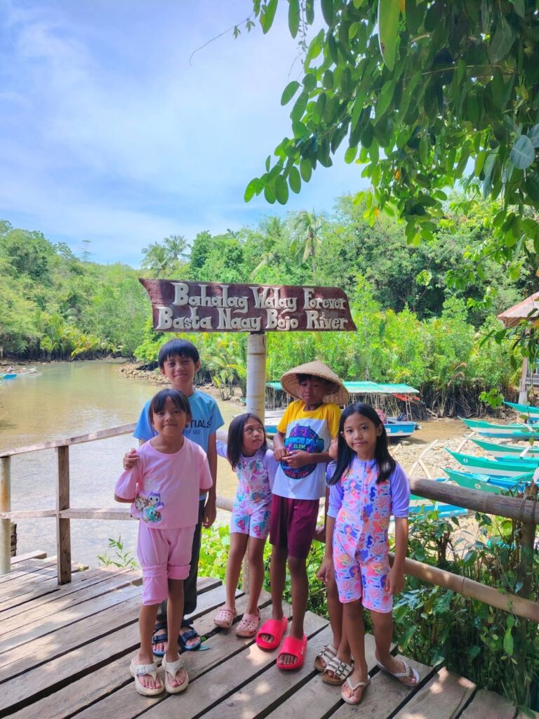 A family on the wooden boardwalk by the river with tour boats behind