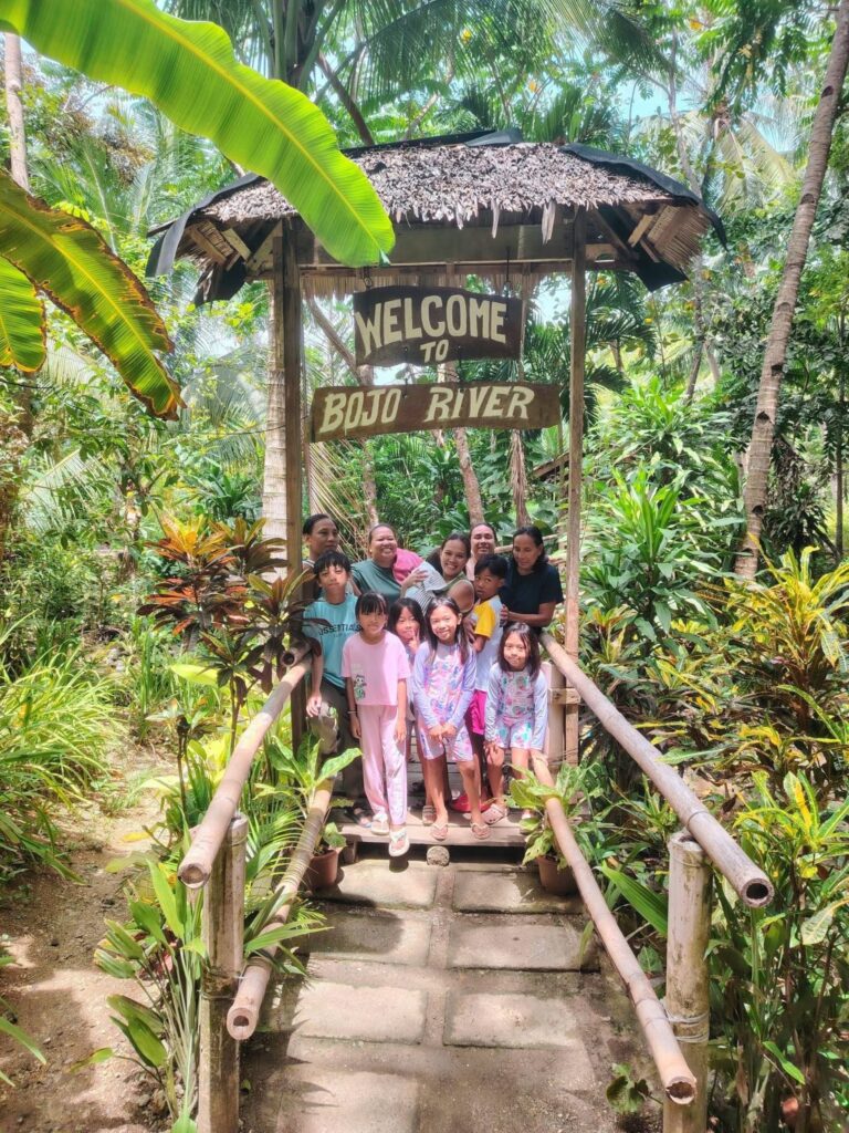 A family under the thatched Welcome to Bojo River arch on the trail