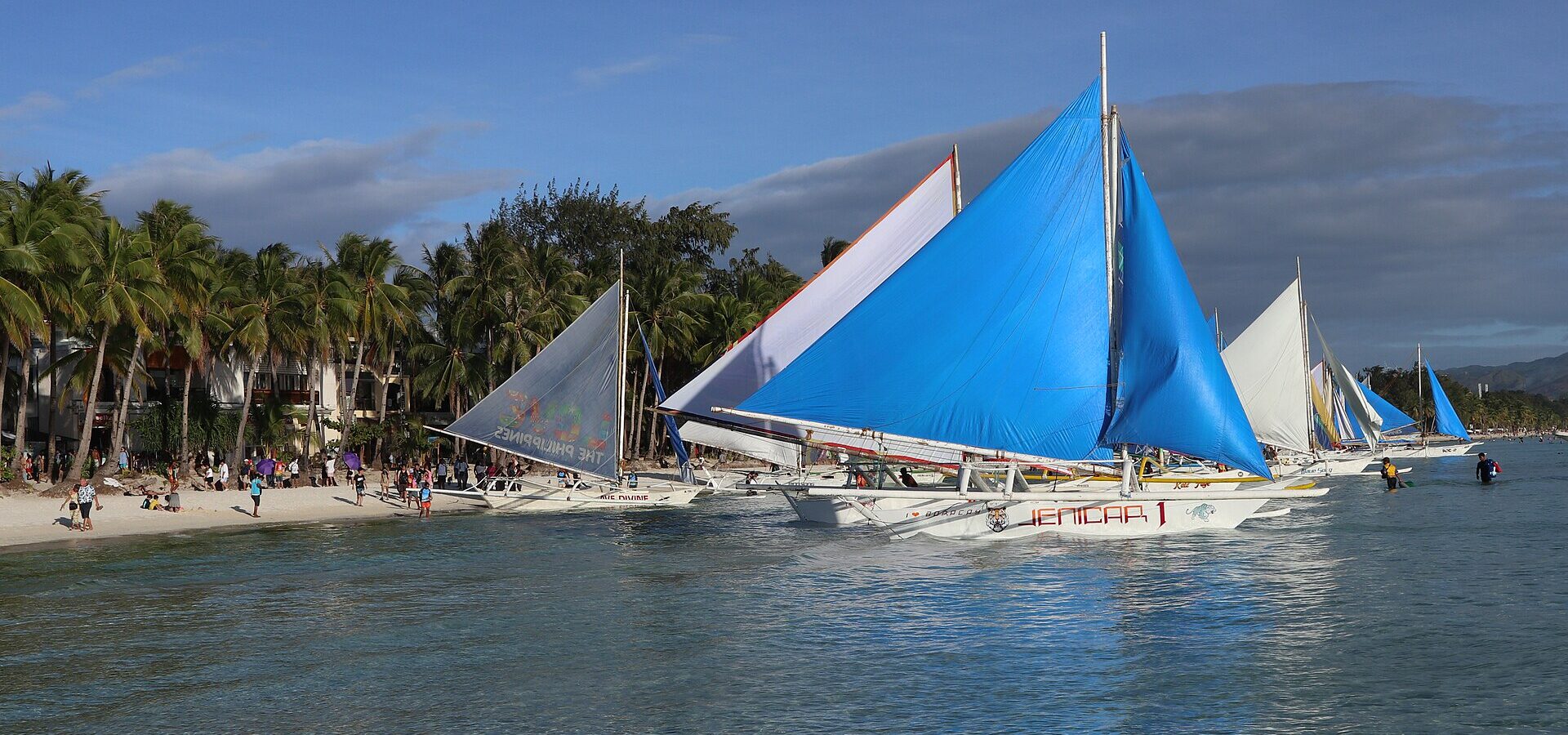 Paraw sailboats with blue and white sails moored off White Beach, Station 2, with palms and clear shallow water