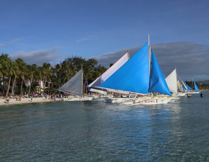 Paraw sailboats with blue and white sails moored off White Beach, Station 2, with palms and clear shallow water