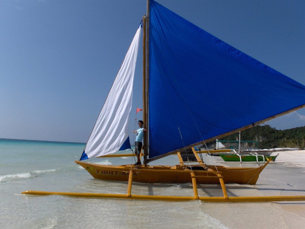 A paraw outrigger sailboat with a blue sail waiting for passengers