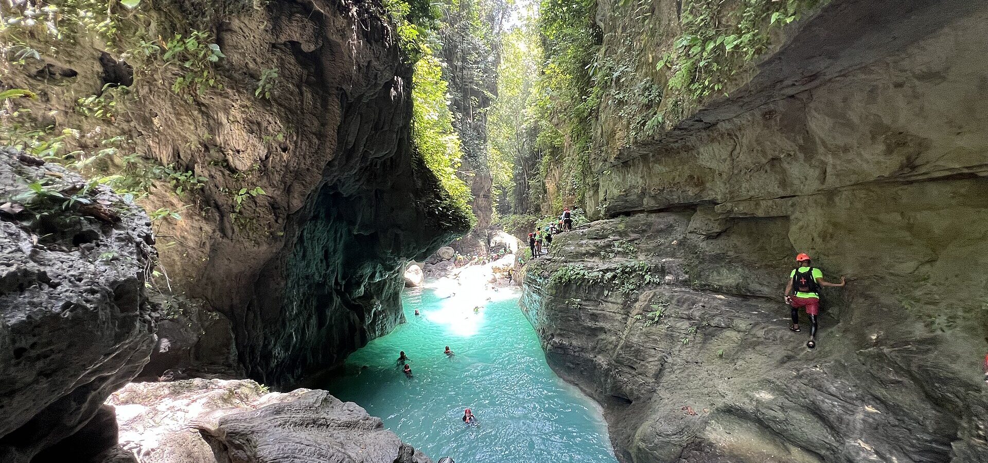 Canyoneers in helmets and life vests in the turquoise Kawasan River canyon, Badian