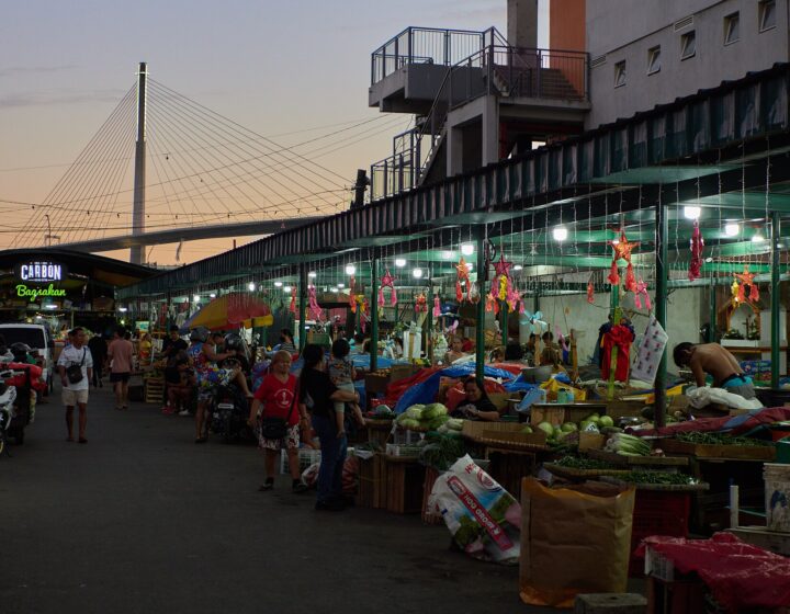 Vendors and vegetable stalls at Carbon Market at dusk, with the Carbon sign and the Marcelo Fernan Bridge behind
