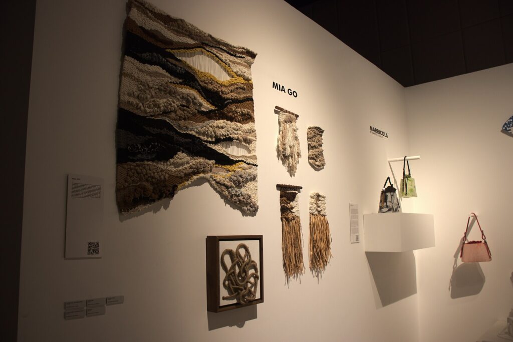 A wall of woven textile art and bags in a changing exhibit