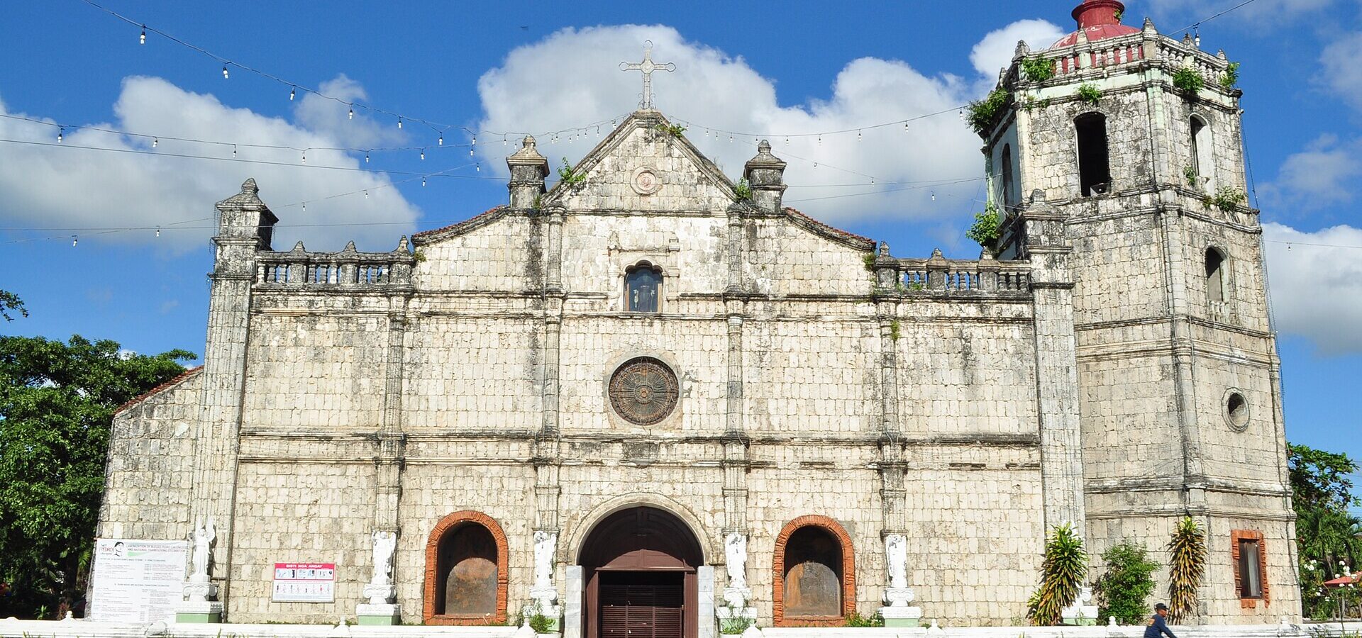Facade and bell tower of the coral-stone Sto. Tomas de Villanueva Church in Danao City under a blue sky