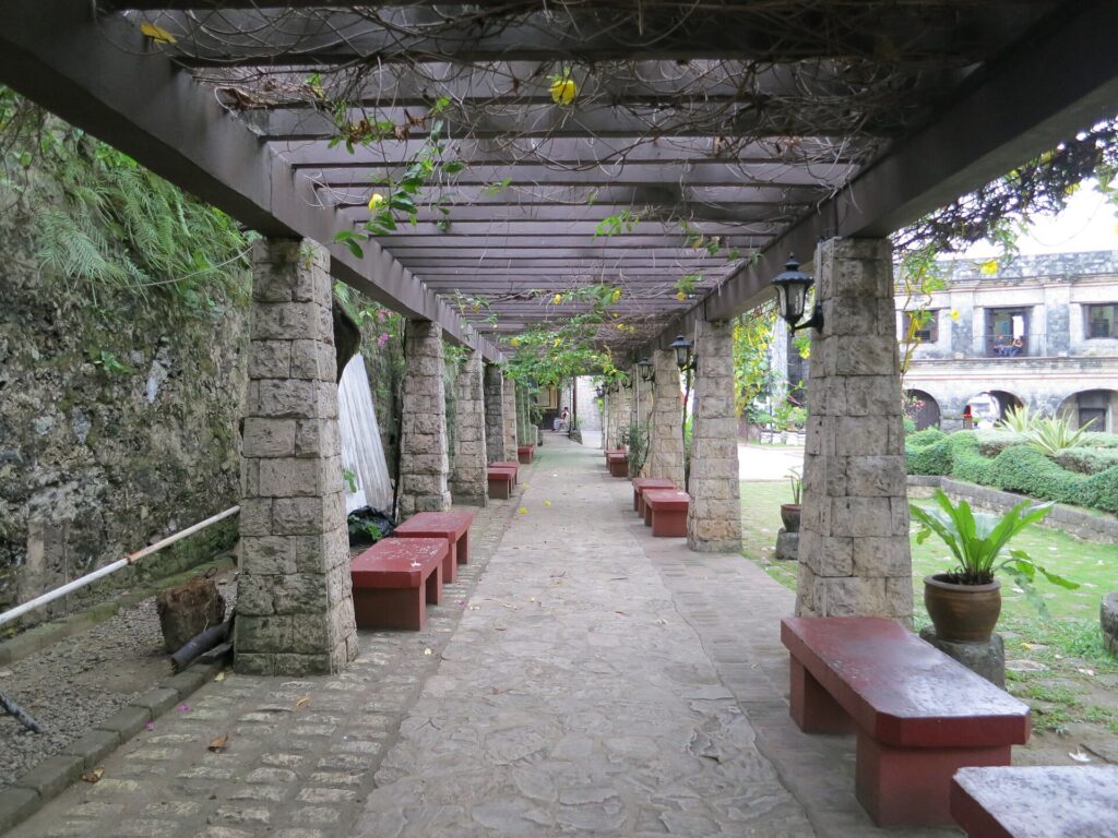 A stone colonnade beside the courtyard, with benches in the shade