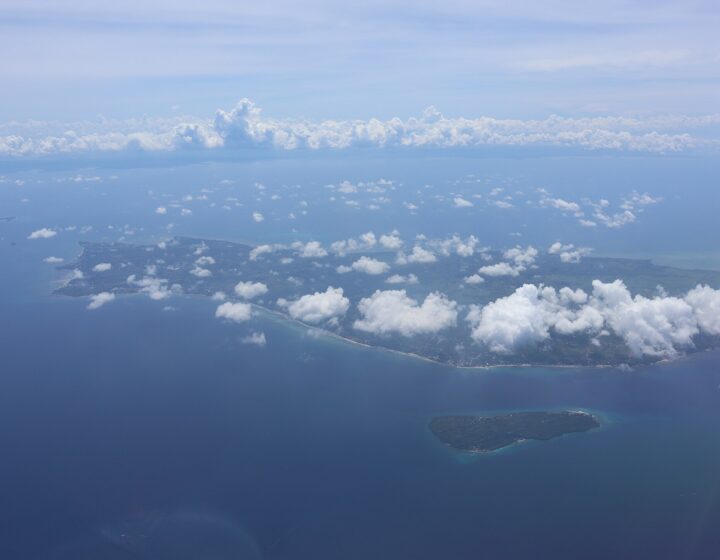 Aerial view from a plane window of a small island (filed as Gibitngil) with the flat north tip of Cebu behind it, under scattered clouds. The only Commons photo of Gibitngil found; the island is small in the frame