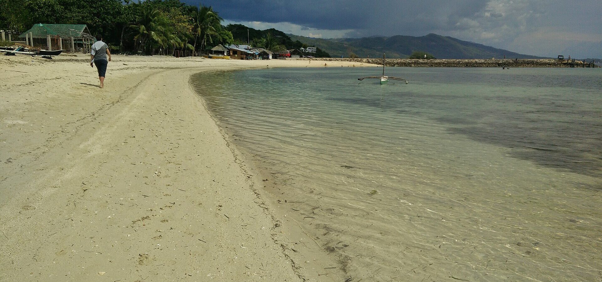 The white sand and clear, shallow water of Lambug Beach in Badian, with palms, cottages and hills behind