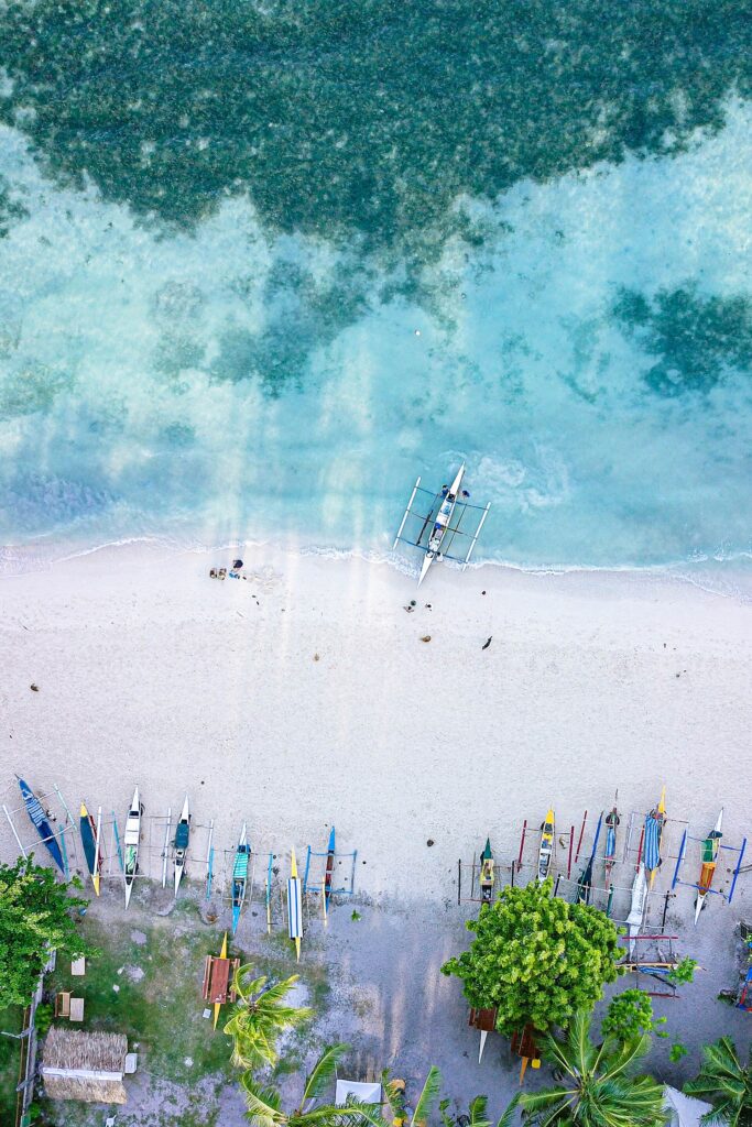 A bangka on the turquoise shallows of Lambug Beach from above