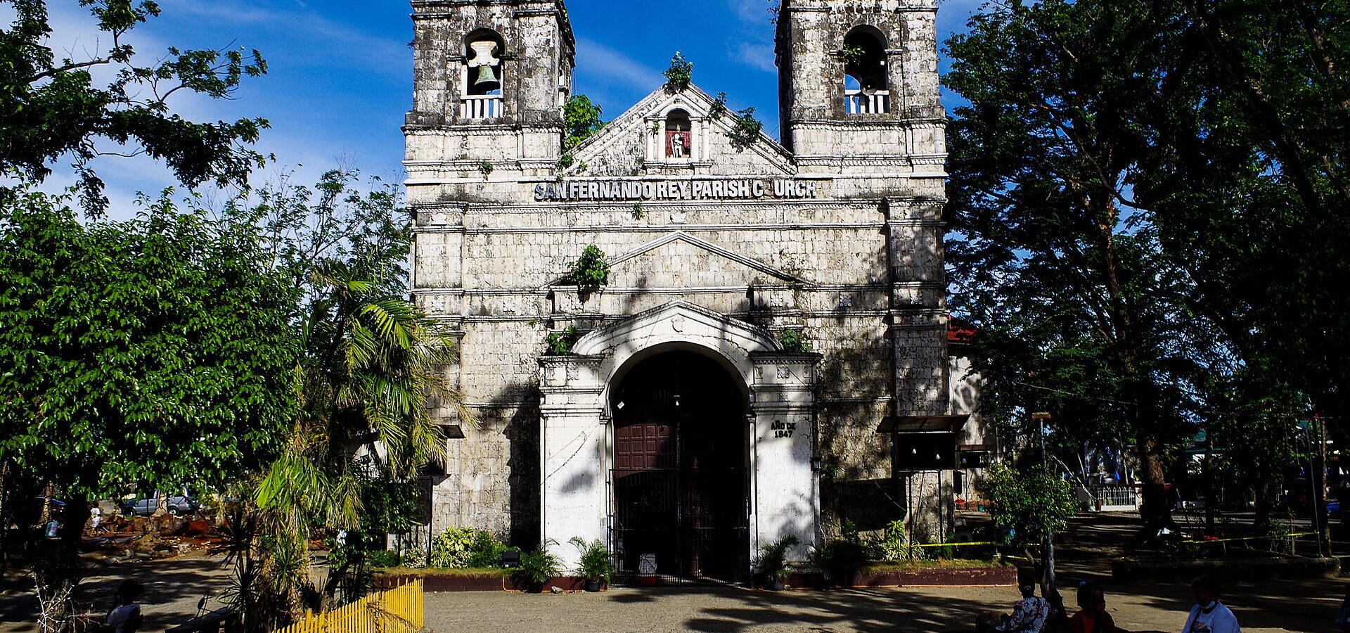 The old stone facade and twin bell towers of San Fernando Rey Parish Church in Liloan, Cebu, under a blue sky