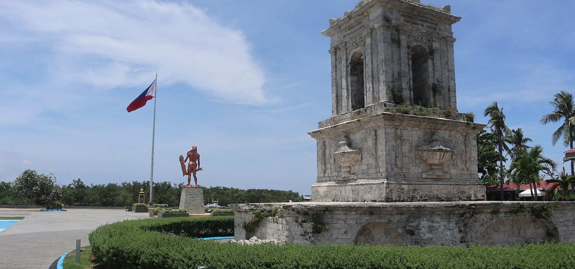 The coral-stone Magellan Monument with the Lapulapu statue and the Philippine flag behind it, Mactan Shrine, 2022