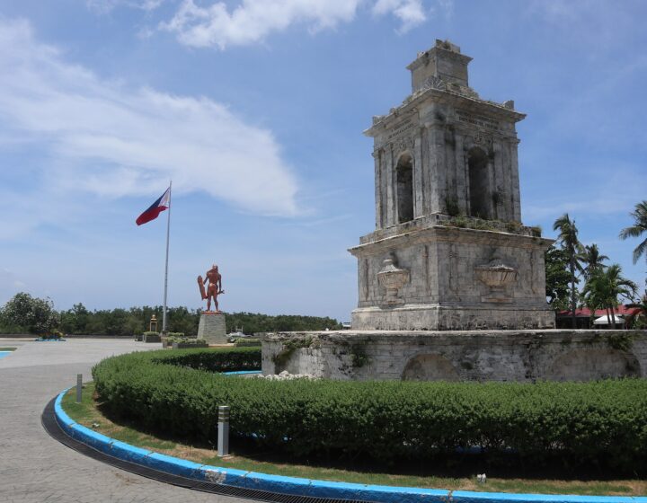 The coral-stone Magellan Monument with the Lapulapu statue and the Philippine flag behind it, Mactan Shrine, 2022