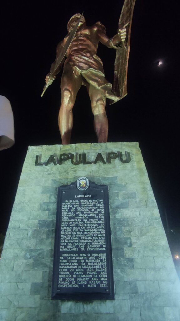 The bronze Lapulapu statue lit up at night, with its historical marker