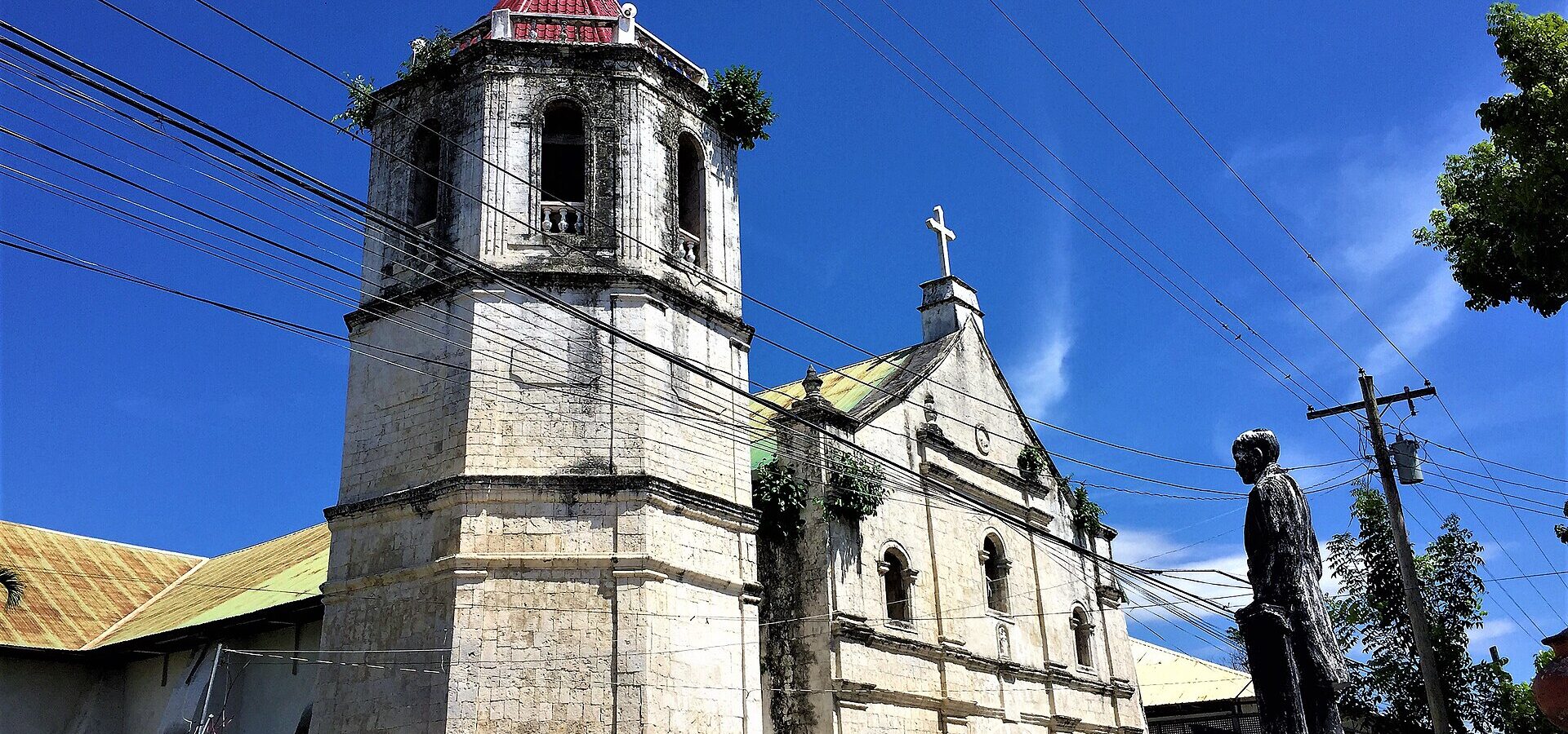 San Nicolas de Tolentino Church in Malabuyoc, with its coral stone bell tower and facade under a blue sky