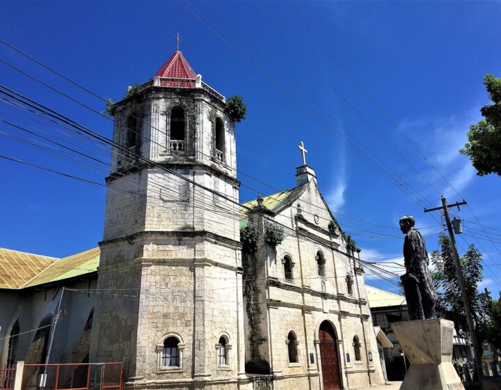 San Nicolas de Tolentino Church in Malabuyoc, with its coral stone bell tower and facade under a blue sky