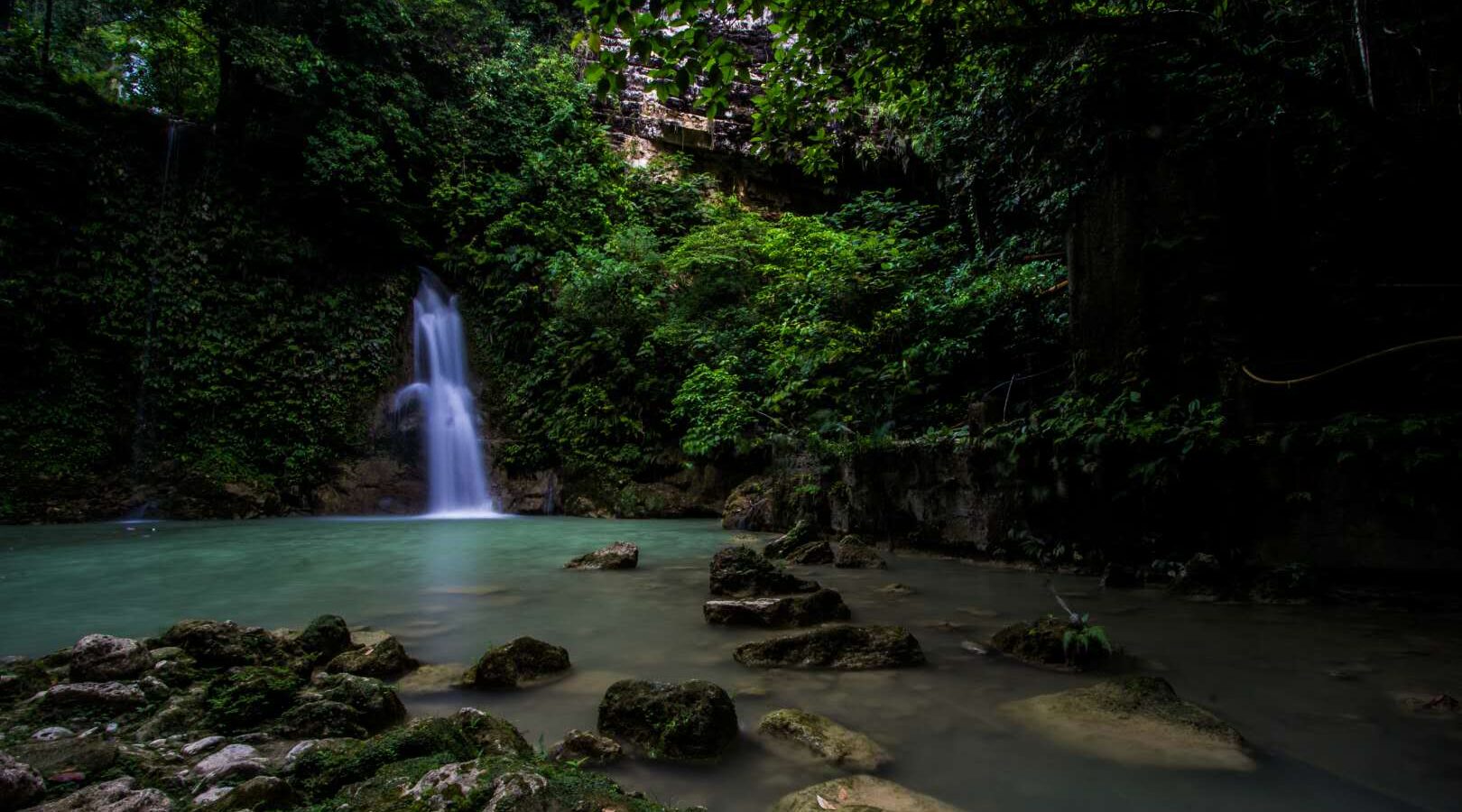 A waterfall at Mantayupan Falls in Barili dropping into a calm green pool surrounded by forest