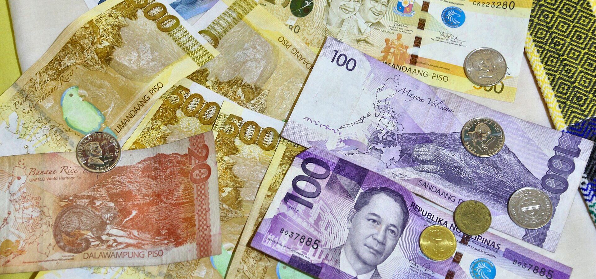Philippine peso banknotes (₱20, ₱100, ₱500, ₱1,000) and coins spread on a table