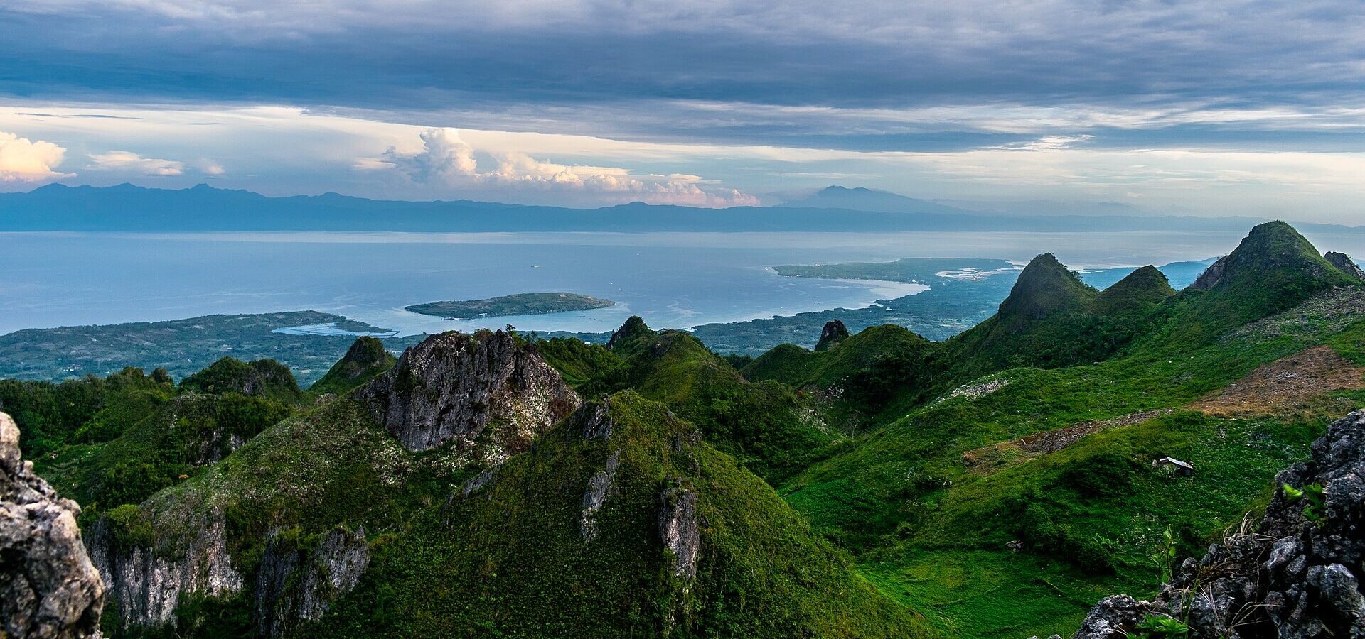View from the top of Osmeña Peak over jagged green hills and the Tañon Strait, with Negros in the background