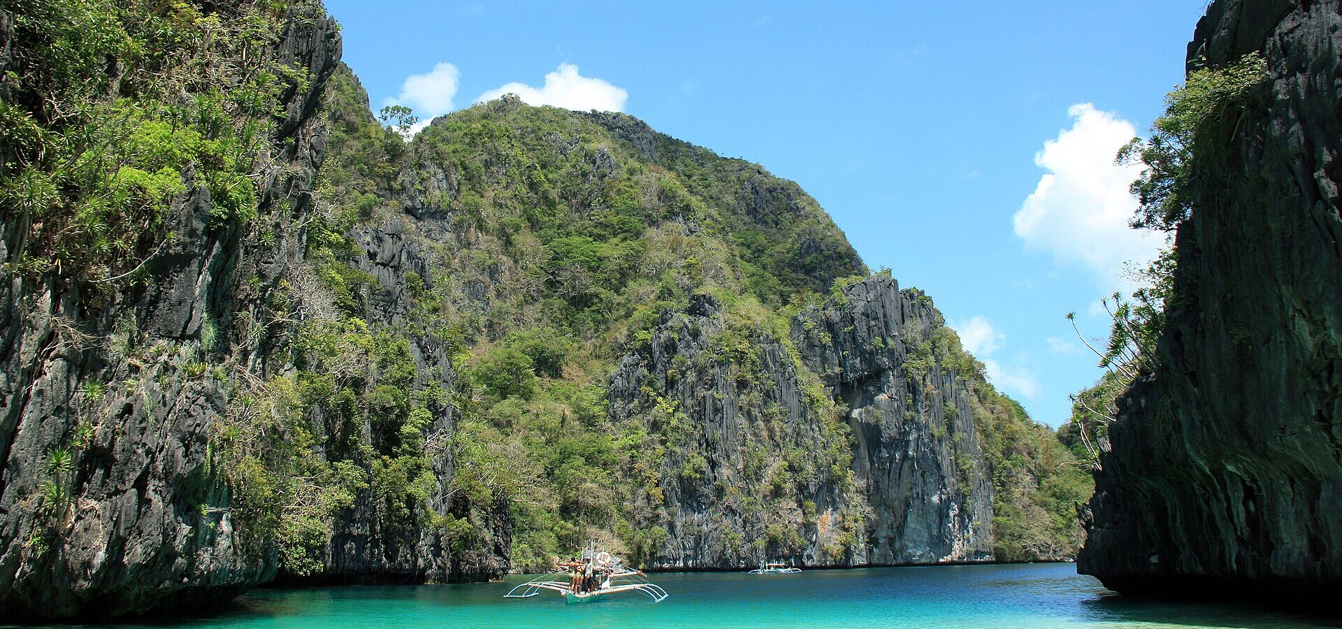 Turquoise water and limestone cliffs at the entrance of the Big Lagoon, El Nido, with an outrigger boat