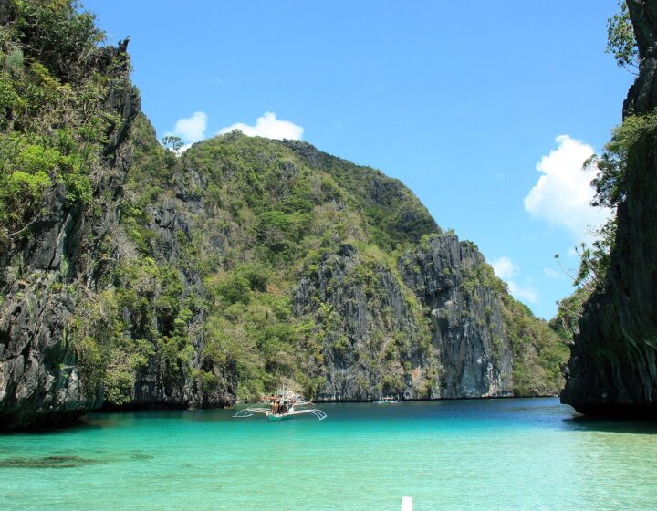 Turquoise water and limestone cliffs at the entrance of the Big Lagoon, El Nido, with an outrigger boat