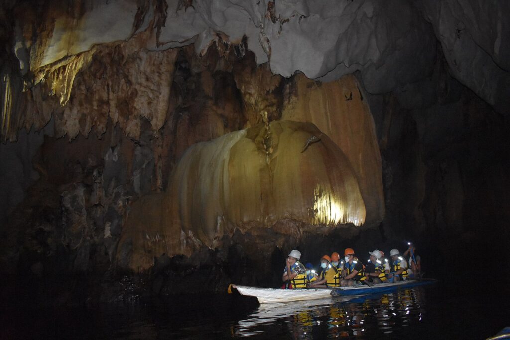 Visitors' boat lit up among the cave formations inside the Underground River