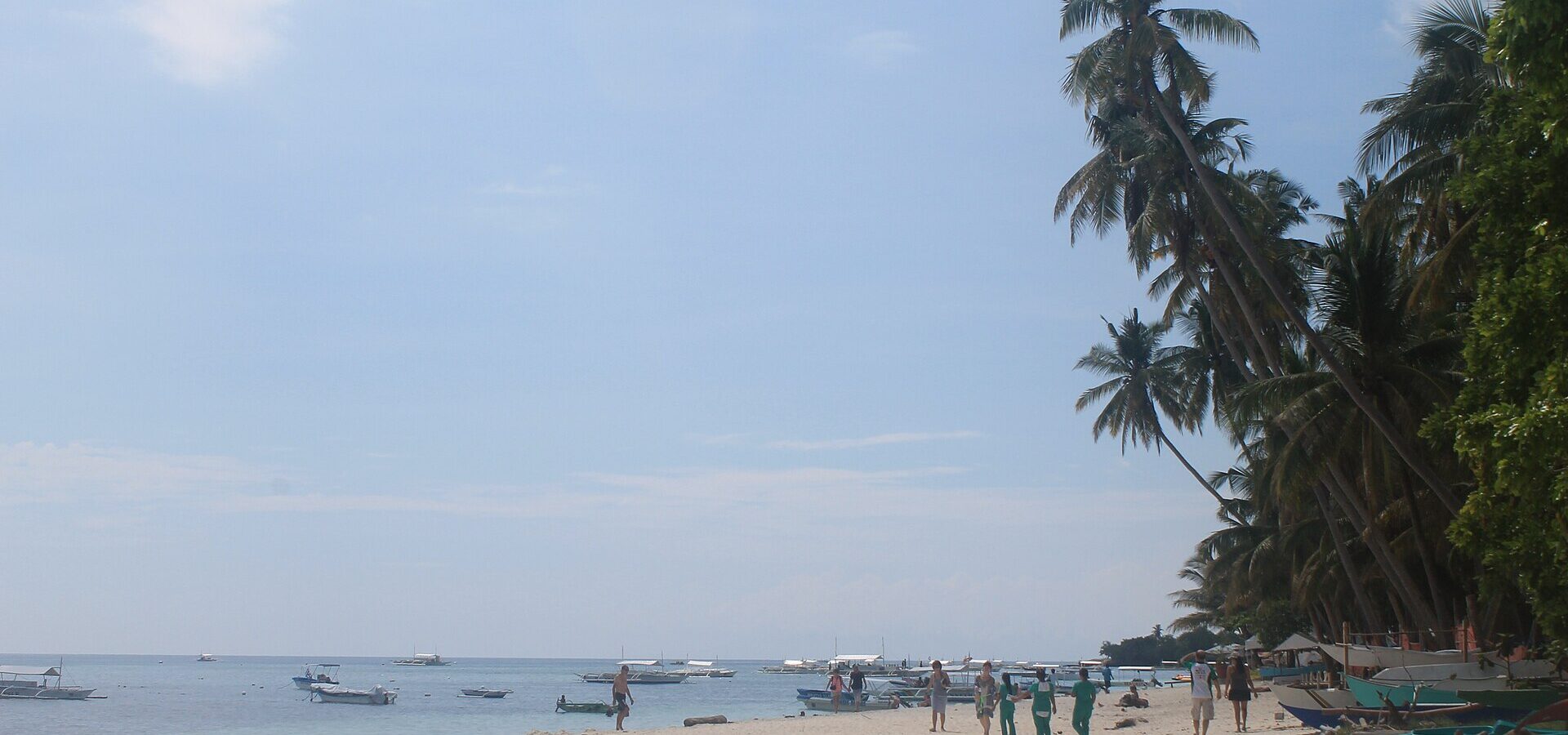 Alona Beach, Panglao: wide white sand, leaning coconut palms and bangka boats moored in calm water under a bright sky