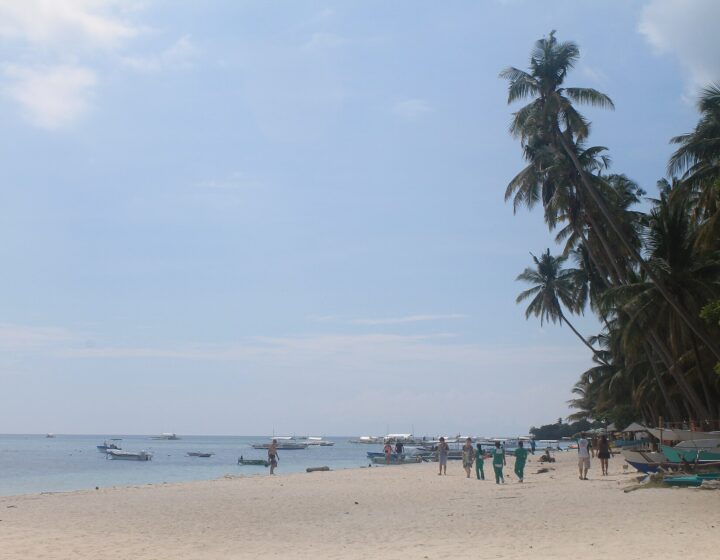 Alona Beach, Panglao: wide white sand, leaning coconut palms and bangka boats moored in calm water under a bright sky