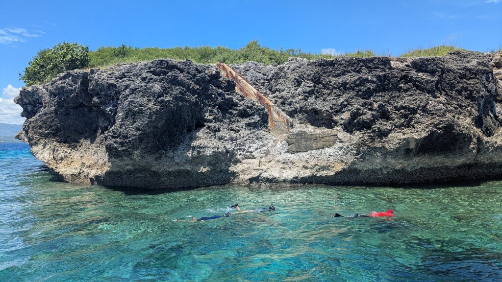 Snorkelers in clear water below the island's rocky cliffs