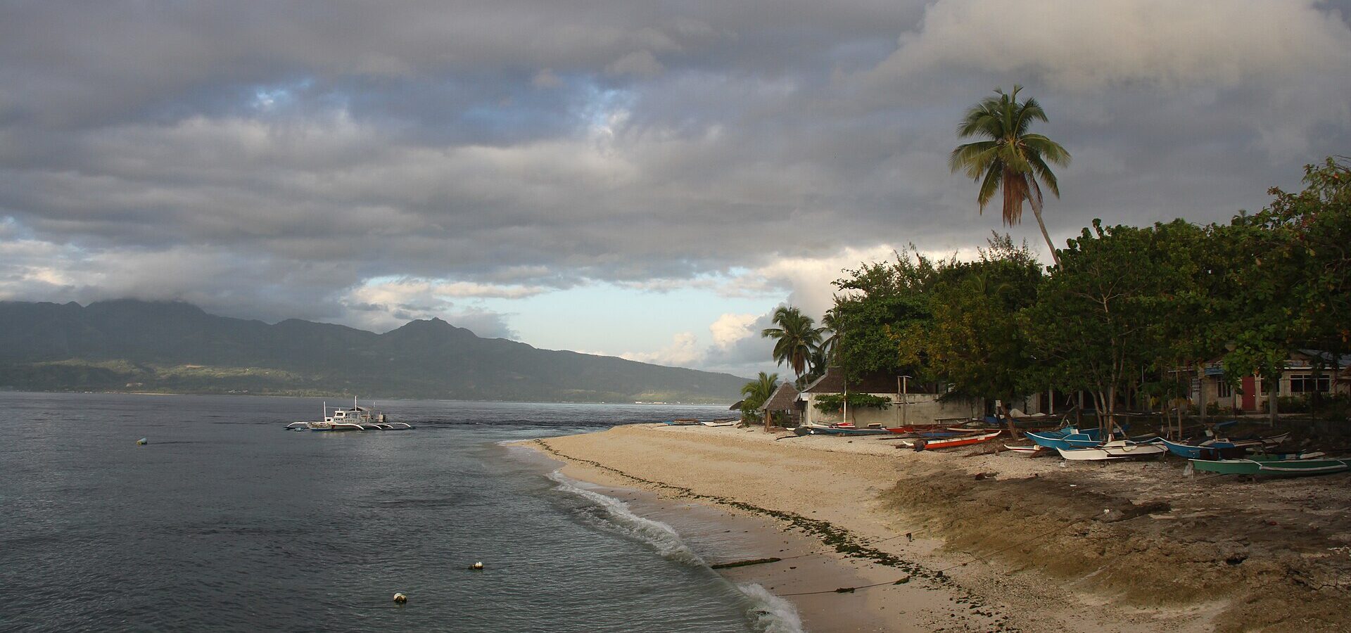 Early morning at Santander port: a curving beach with palms and outrigger boats, and the mountains of Negros across the strait
