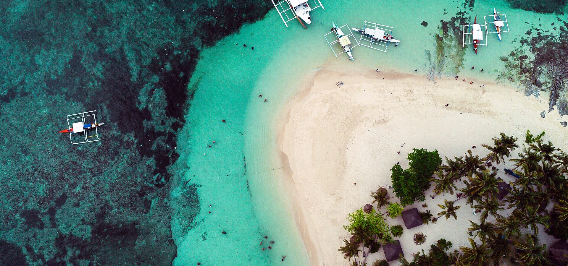 Aerial view of Guyam Island: white sand, palms and outrigger boats on turquoise water