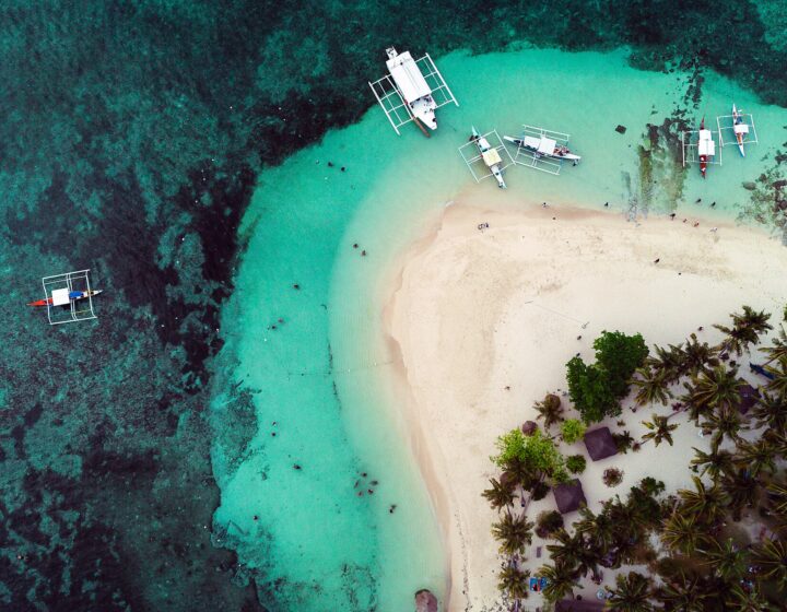 Aerial view of Guyam Island: white sand, palms and outrigger boats on turquoise water