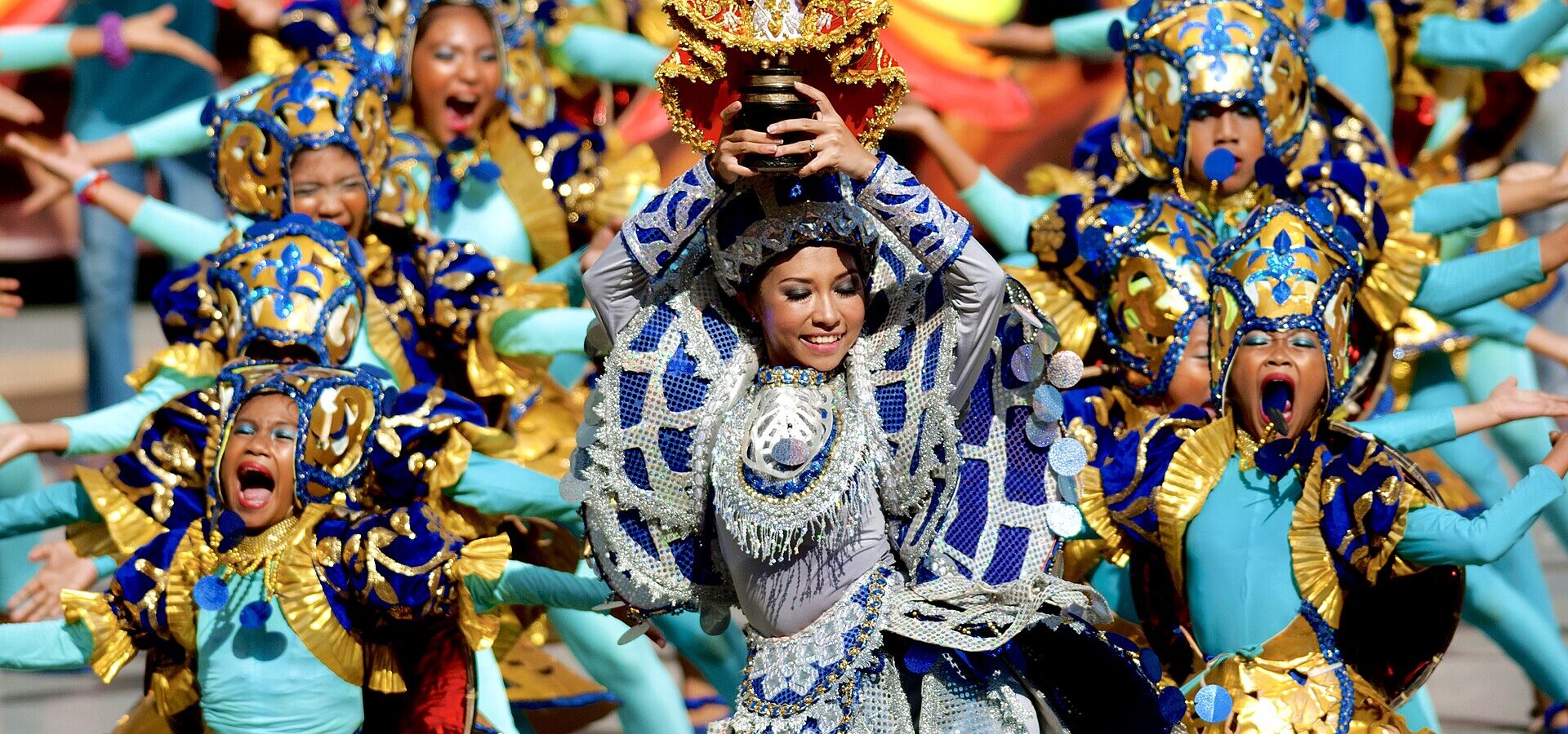 Sinulog Festival dancers in colourful blue and gold costumes, one holding up an image of the Santo Niño