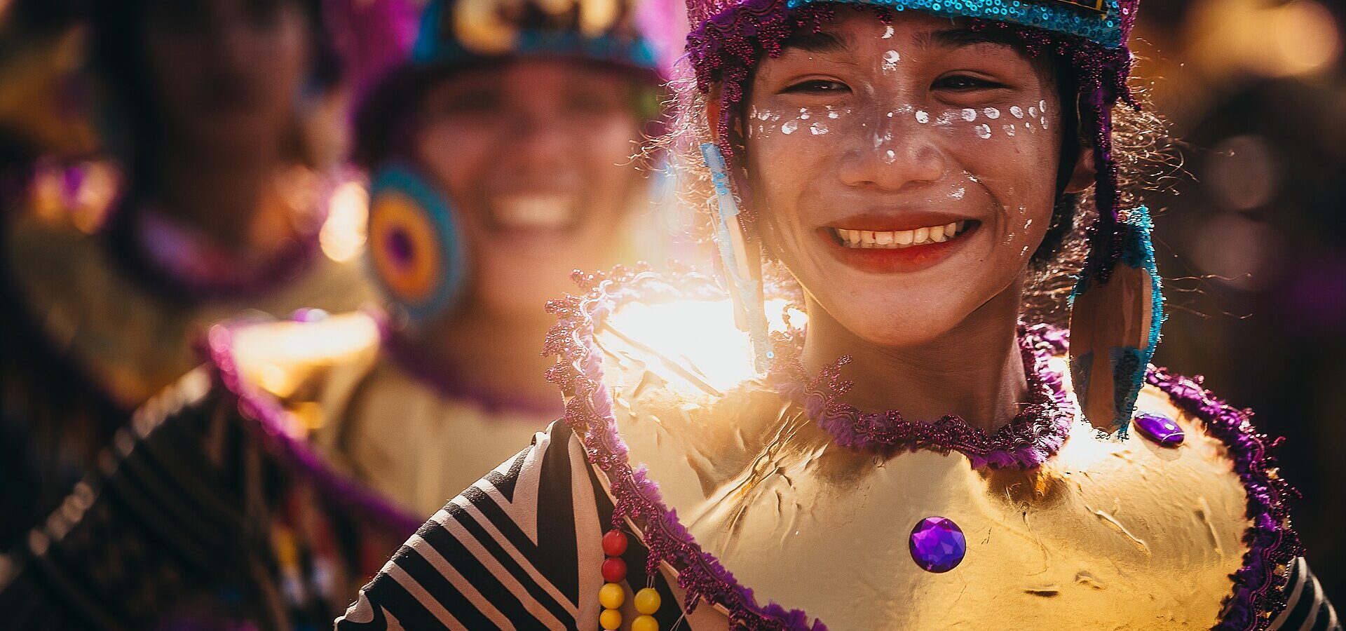 A smiling Sinulog dancer in a bright costume and face paint during the 2023 street dance in Cebu City