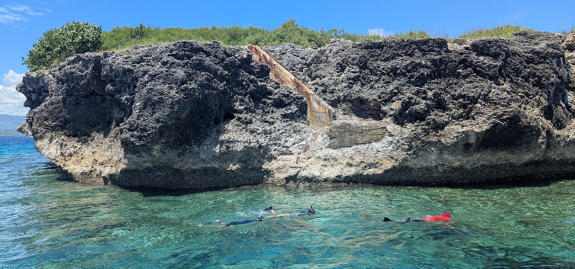 Snorkellers in clear turquoise water beside the rocky edge of Pescador Island, Moalboal