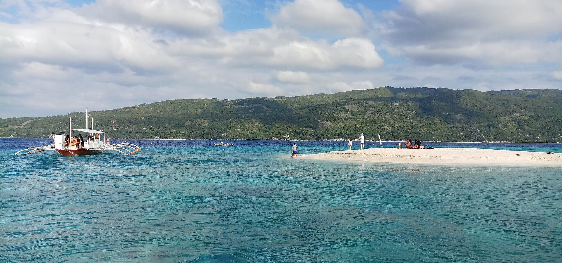 The white sandbar of Sumilon Island reaching out into the sea, with the mainland of Cebu in the background