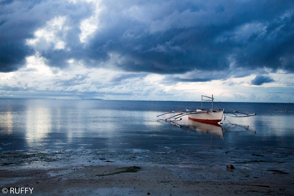 An outrigger boat on the calm sea off the Alcoy shore at dawn
