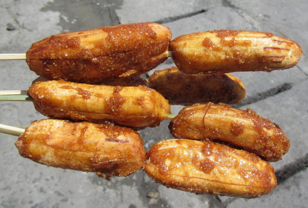 Four sticks of caramelised fried banana cue held on bamboo skewers