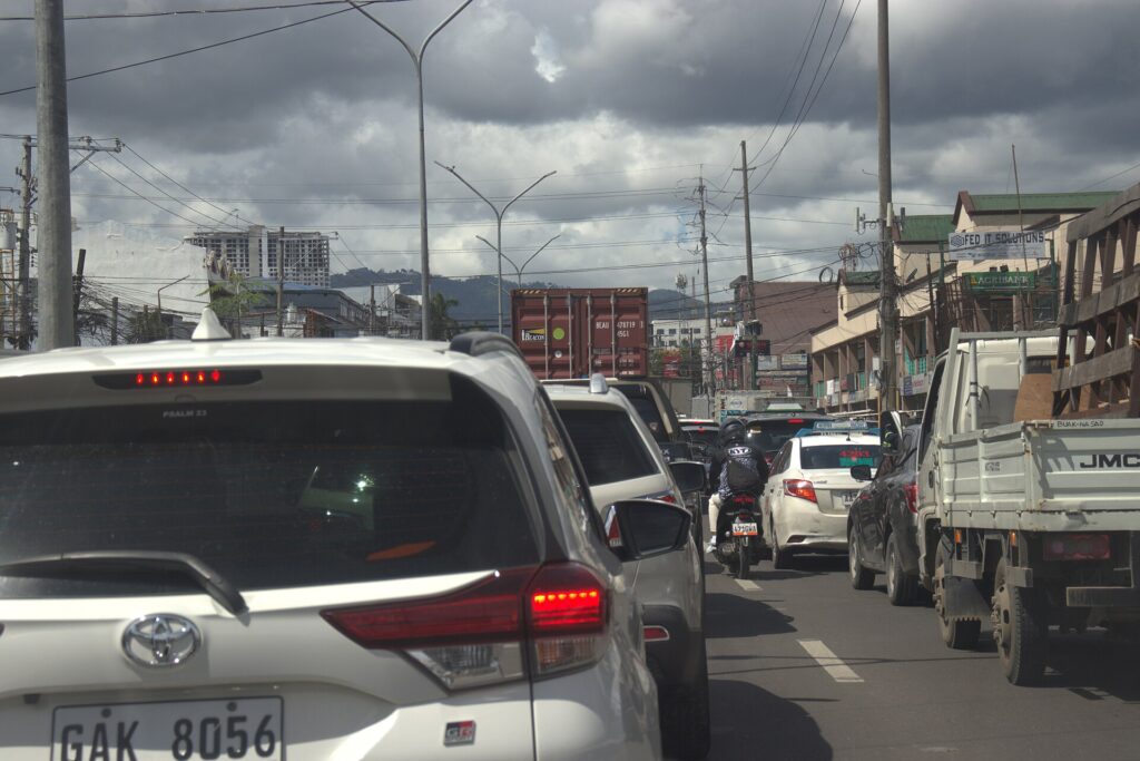 A line of cars and trucks stuck in slow traffic on a busy Cebu City road under grey clouds
