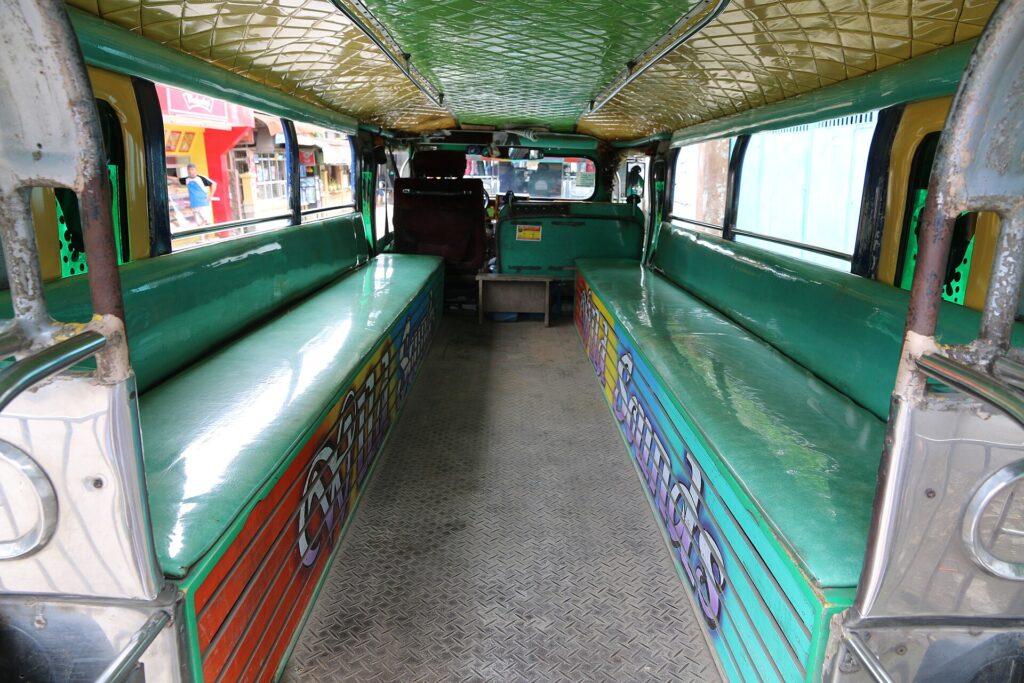 The inside of an empty jeepney with two long green padded benches facing each other