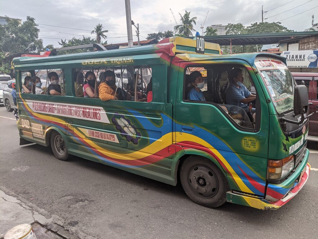 A green and yellow jeepney with a route code on its windscreen and passengers inside, on a Cebu City street