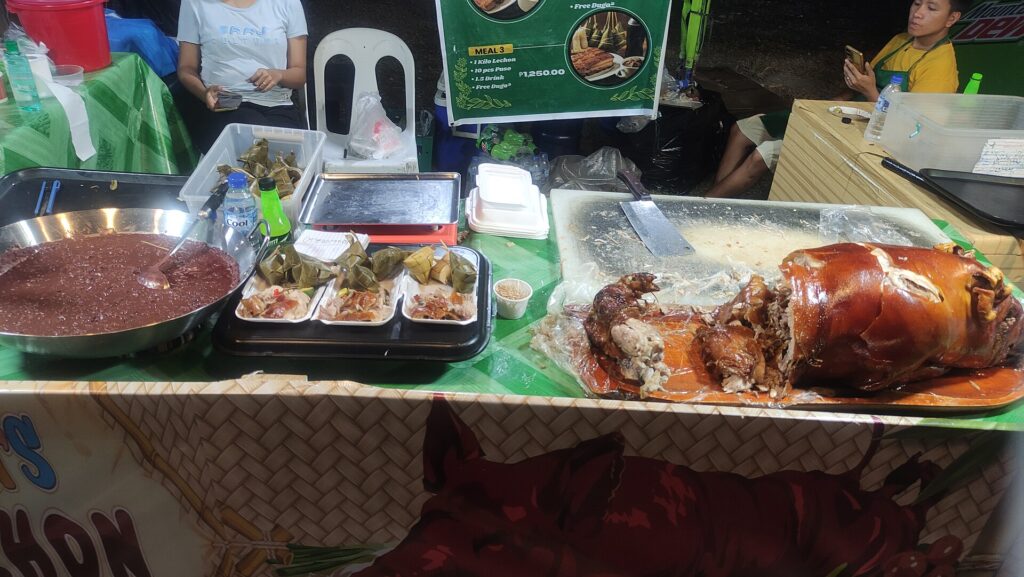 A food stall counter with roast lechon pork and dishes on banana leaves