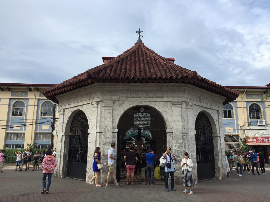 The small stone pavilion that holds Magellan's Cross in Cebu City, with visitors standing in front