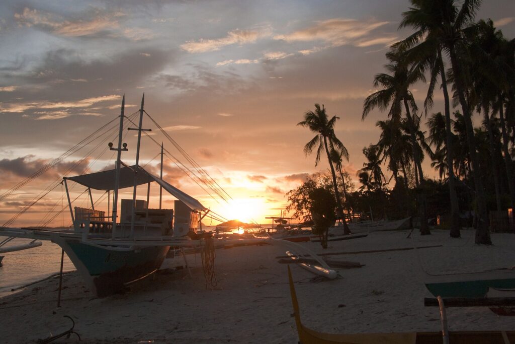 A golden sunset behind palm trees and a moored bangka on the beach at Malapascua