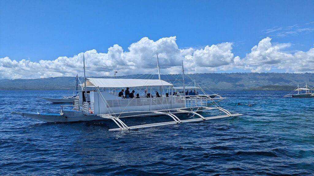 A white outrigger tour boat with passengers on deck on blue water off Moalboal, Cebu