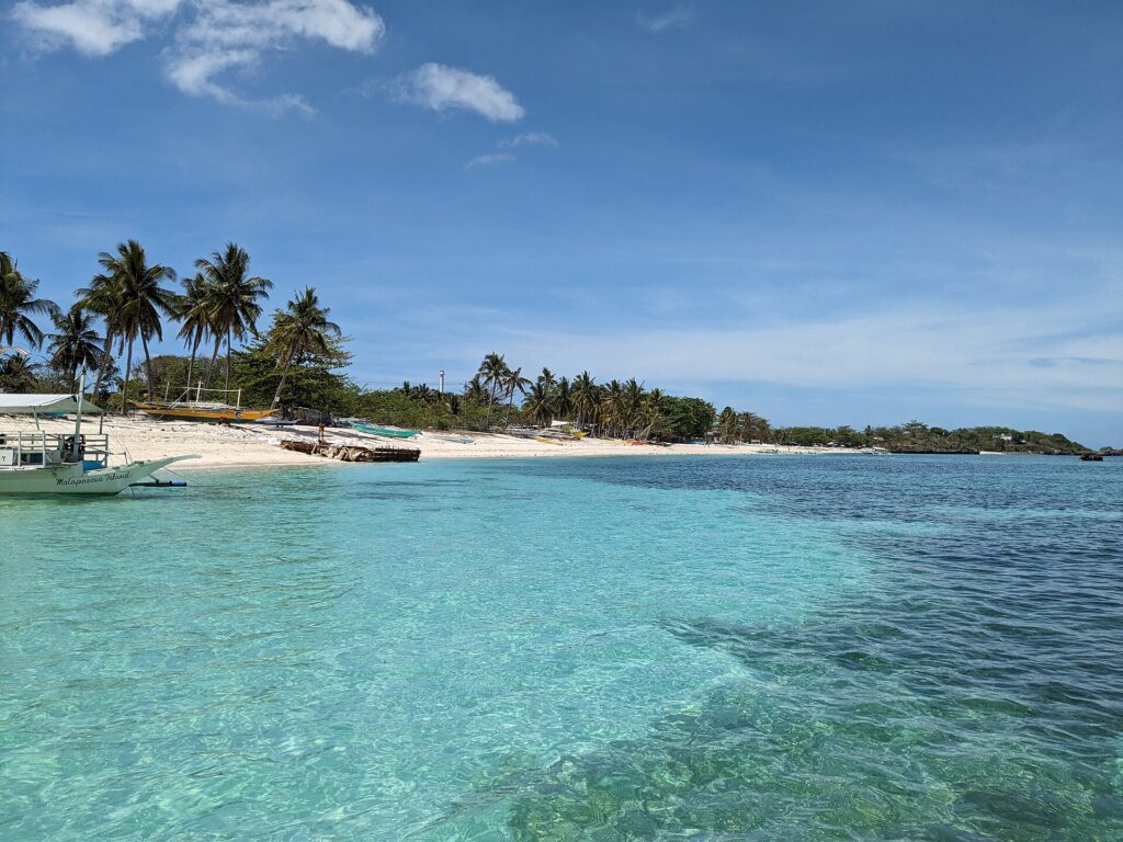 Clear turquoise water and a palm-fringed white sand beach on Malapascua island with a bangka boat at the shore