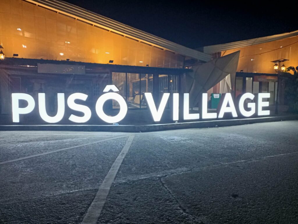The lit Puso Village sign at night in front of a food hall in Cebu City